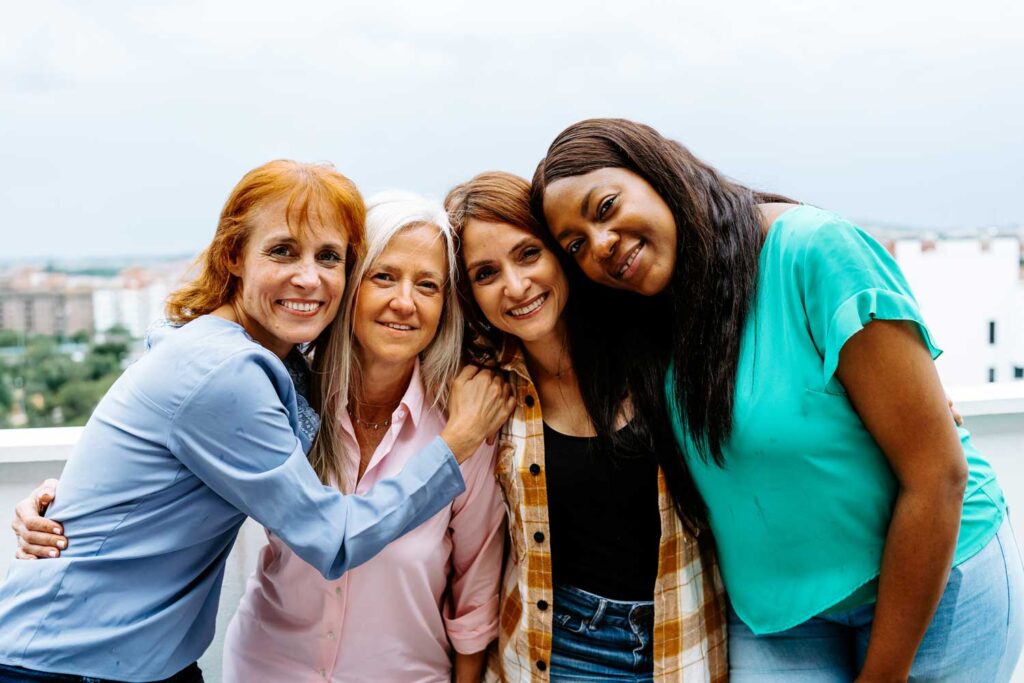 Four diverse women smiling closely together, embodying friendship and support, perhaps symbolizing a strong support network for women's wellness and mental health.