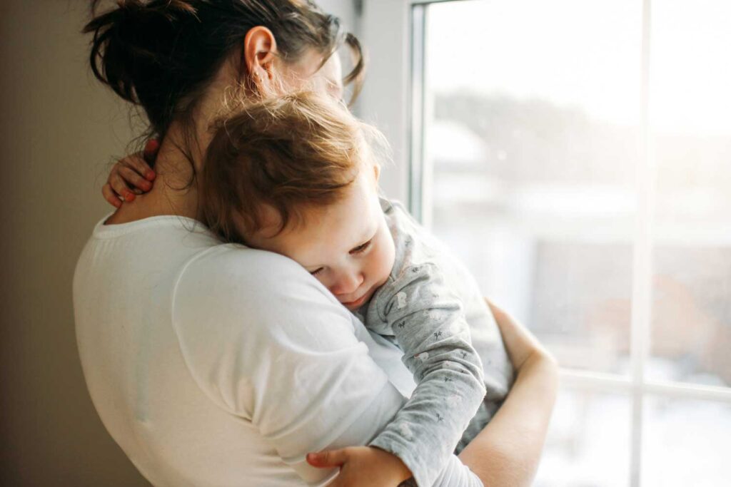 A comforting embrace between a mother and her toddler in a softly lit room, embodying the warmth of maternal love.