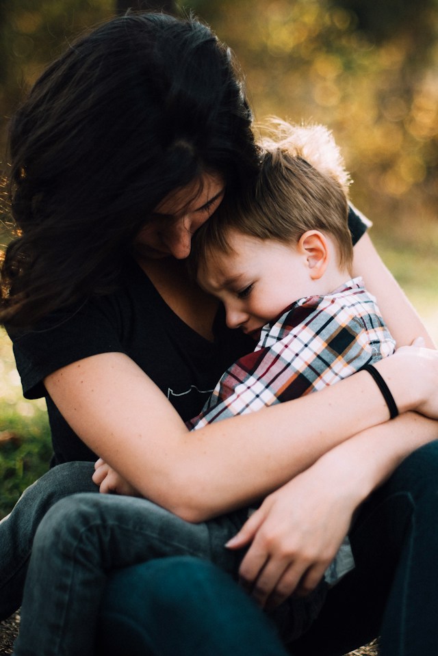 A tender moment as a mother lovingly embraces her young son in a warm, outdoor setting.